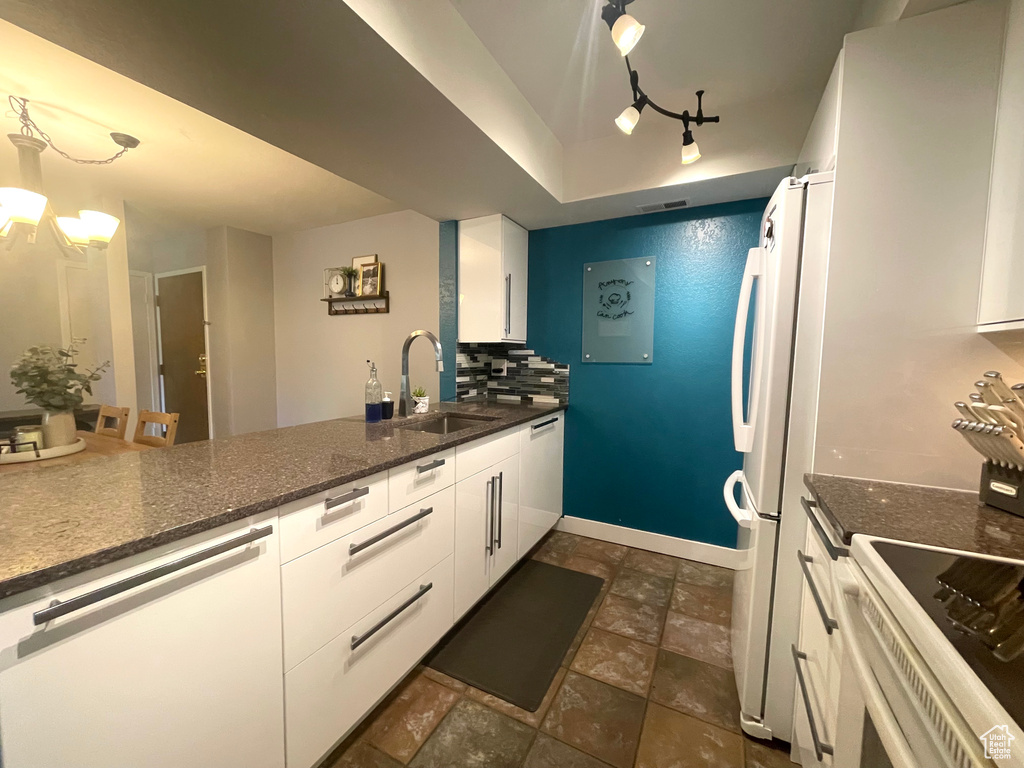 Kitchen with white appliances, white cabinetry, dark stone finish flooring, and rail lighting