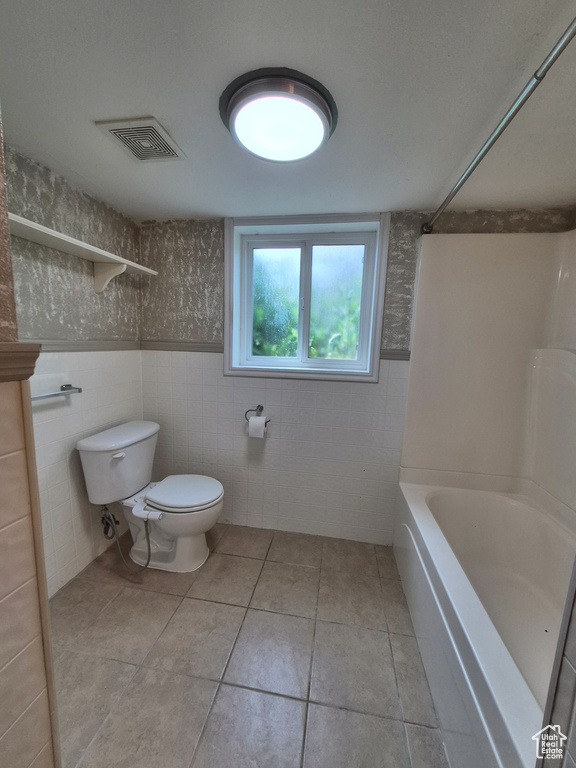 Bathroom featuring tile walls, tile patterned flooring, shower / washtub combination, and wainscoting
