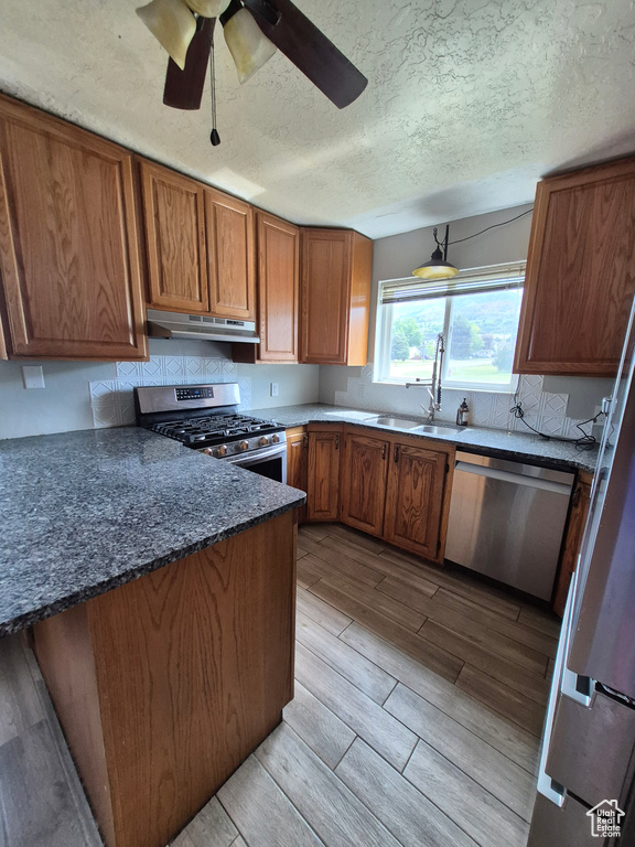 Kitchen featuring stainless steel appliances, under cabinet range hood, brown cabinetry, a ceiling fan, and wood tiled floors