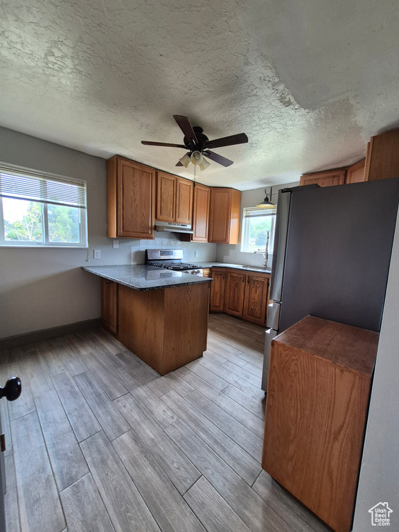Kitchen featuring appliances with stainless steel finishes, a peninsula, brown cabinets, plenty of natural light, and a textured ceiling