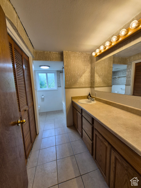Bathroom featuring vanity, a textured ceiling, tile patterned flooring, tile walls, and a closet