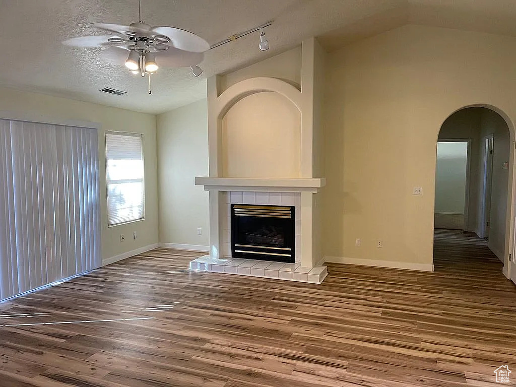 Unfurnished living room featuring ceiling fan, wood finished floors, a fireplace, arched walkways, and rail lighting