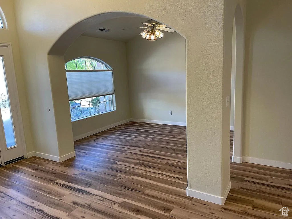 Unfurnished room with ceiling fan, wood finished floors, and arched walkways