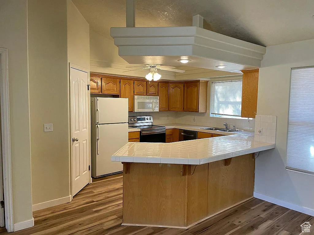 Kitchen with white appliances, a peninsula, wood finished floors, and tile countertops