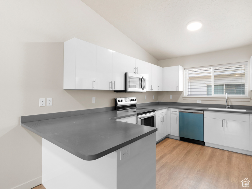 Kitchen with appliances with stainless steel finishes, a peninsula, dark countertops, lofted ceiling, and white cabinets