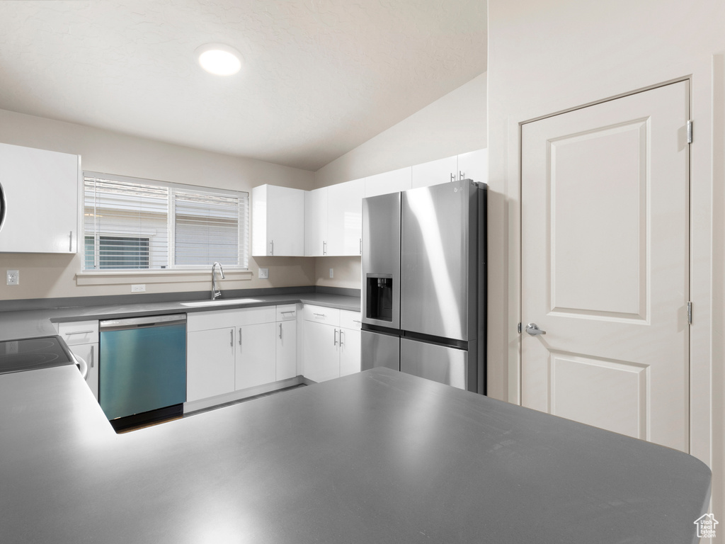 Kitchen featuring stainless steel appliances, vaulted ceiling, white cabinets, and dark countertops