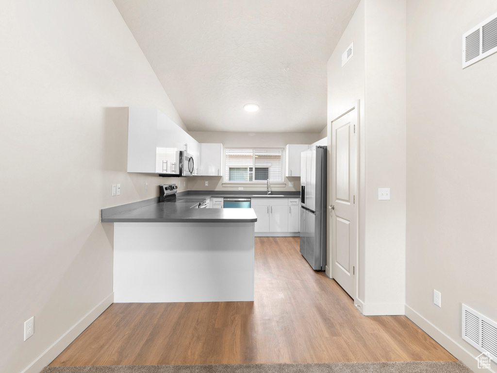 Kitchen featuring appliances with stainless steel finishes, a peninsula, dark countertops, white cabinets, and light wood finished floors
