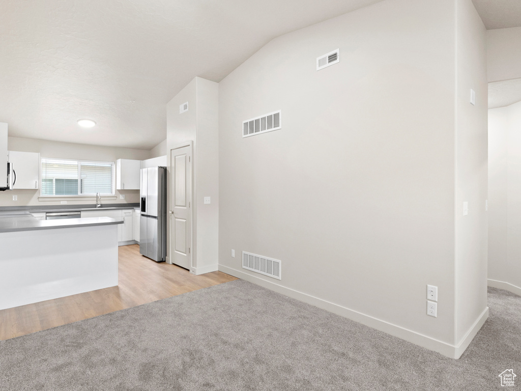 Kitchen featuring appliances with stainless steel finishes, light colored carpet, white cabinets, vaulted ceiling, and a peninsula