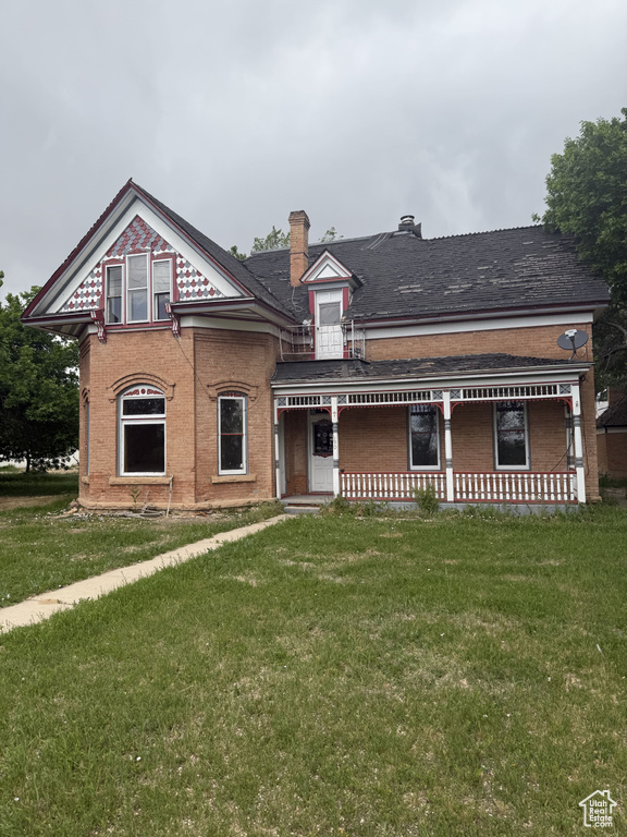Victorian home with covered porch, a front yard, brick siding, and a chimney