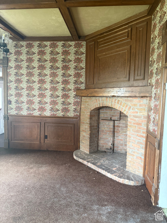 Unfurnished living room with wallpapered walls, a wainscoted wall, carpet, a wood stove, and coffered ceiling