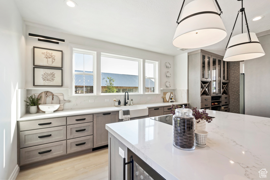 Kitchen with light stone counters, light wood-style flooring, hanging light fixtures, decorative backsplash, and recessed lighting