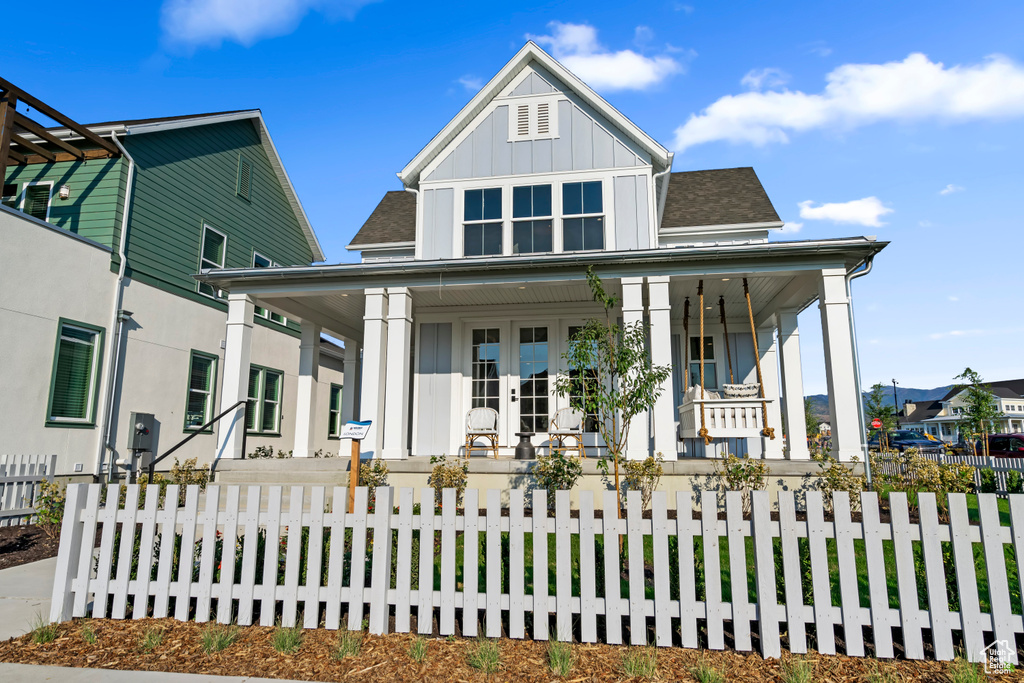 View of front of house with covered porch, board and batten siding, a fenced front yard, and roof with shingles
