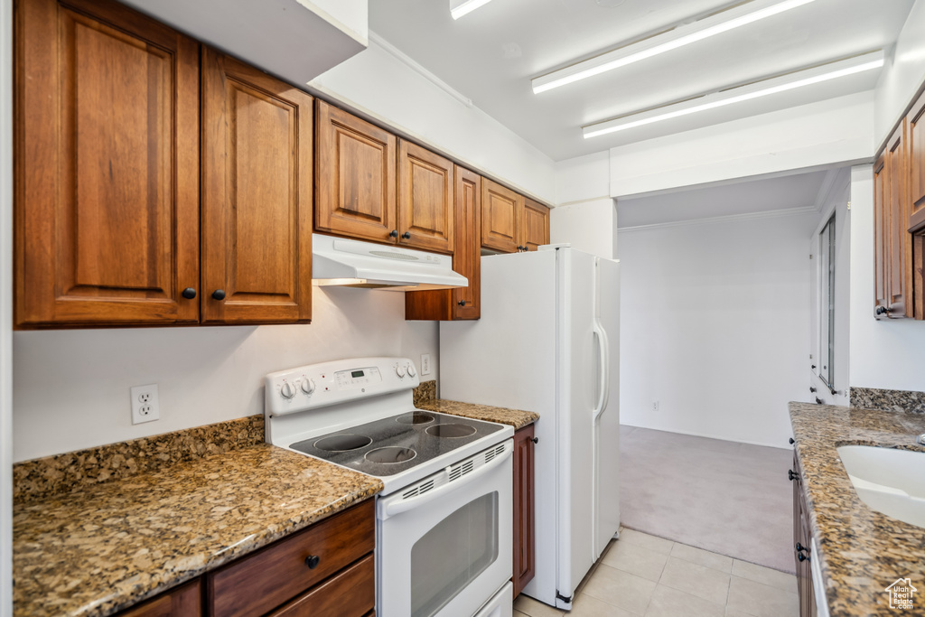 Kitchen with electric range, under cabinet range hood, brown cabinets, light carpet, and light tile patterned floors