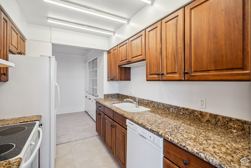 Kitchen featuring white appliances, light colored carpet, brown cabinetry, and stone countertops