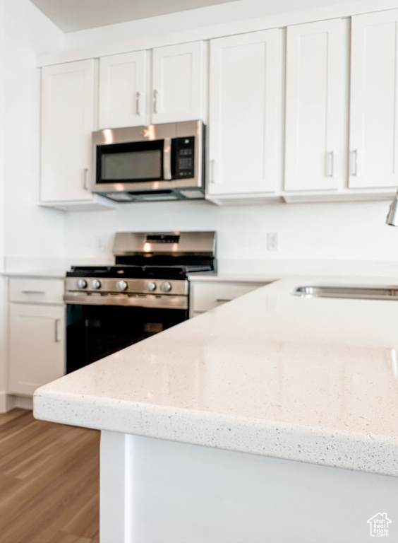 Kitchen with stainless steel appliances, white cabinets, light wood-style floors, and light stone countertops