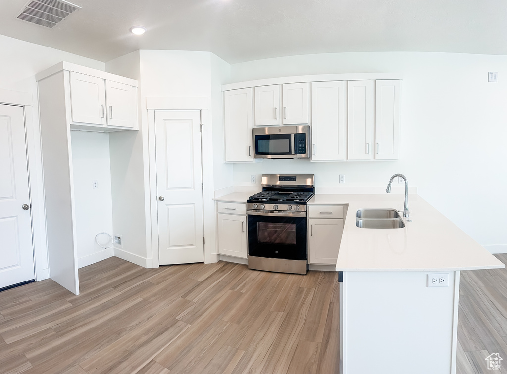 Kitchen featuring stainless steel appliances, a peninsula, light wood-style flooring, light countertops, and white cabinetry