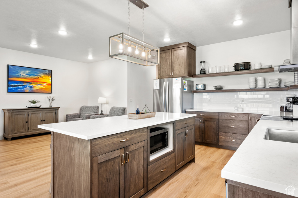 Kitchen featuring freestanding refrigerator, light wood-style flooring, open shelves, light countertops, and a center island