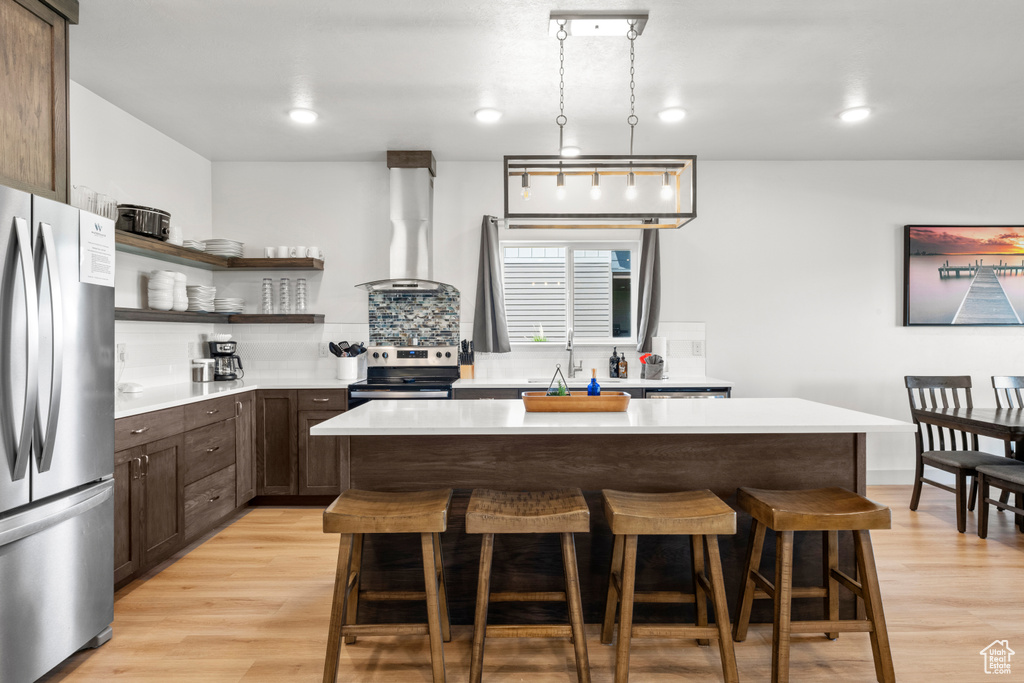 Kitchen with appliances with stainless steel finishes, extractor fan, a breakfast bar area, dark brown cabinets, and light wood-style flooring