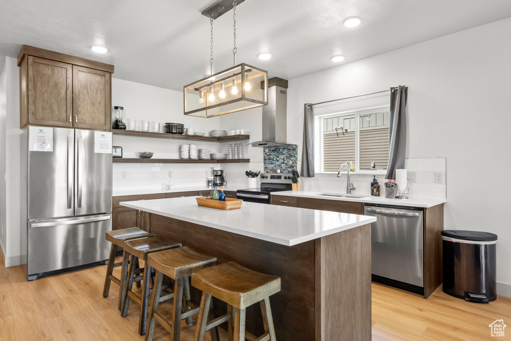 Kitchen with appliances with stainless steel finishes, extractor fan, open shelves, light wood finished floors, and recessed lighting