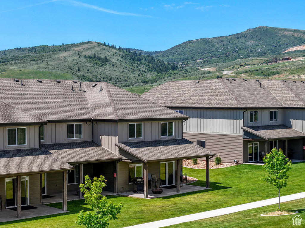 Rear view of property featuring a patio area, board and batten siding, a mountain view, a yard, and roof with shingles