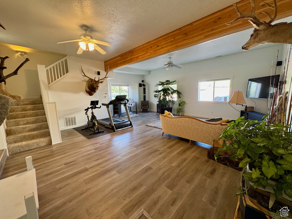 Living area with a ceiling fan, beam ceiling, wood finished floors, stairway, and a textured ceiling