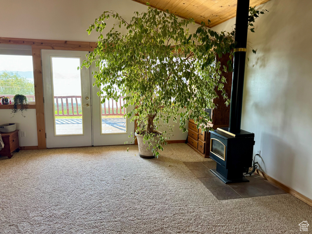 Unfurnished living room featuring carpet, a wood stove, vaulted ceiling, and wood ceiling