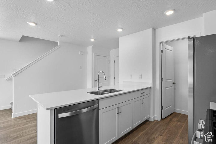 Kitchen featuring appliances with stainless steel finishes, a peninsula, a textured ceiling, dark wood finished floors, and light countertops
