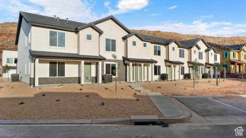 Townhome / multi-family property with stucco siding, brick siding, a residential view, and uncovered parking