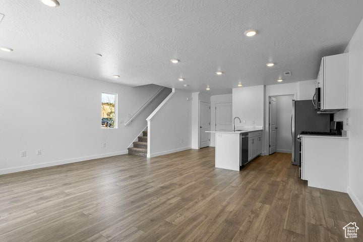 Kitchen with open floor plan, appliances with stainless steel finishes, wood finished floors, a textured ceiling, and white cabinets