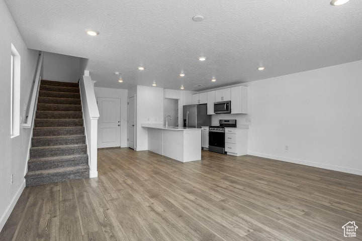 Unfurnished living room featuring wood finished floors, stairway, recessed lighting, and a textured ceiling