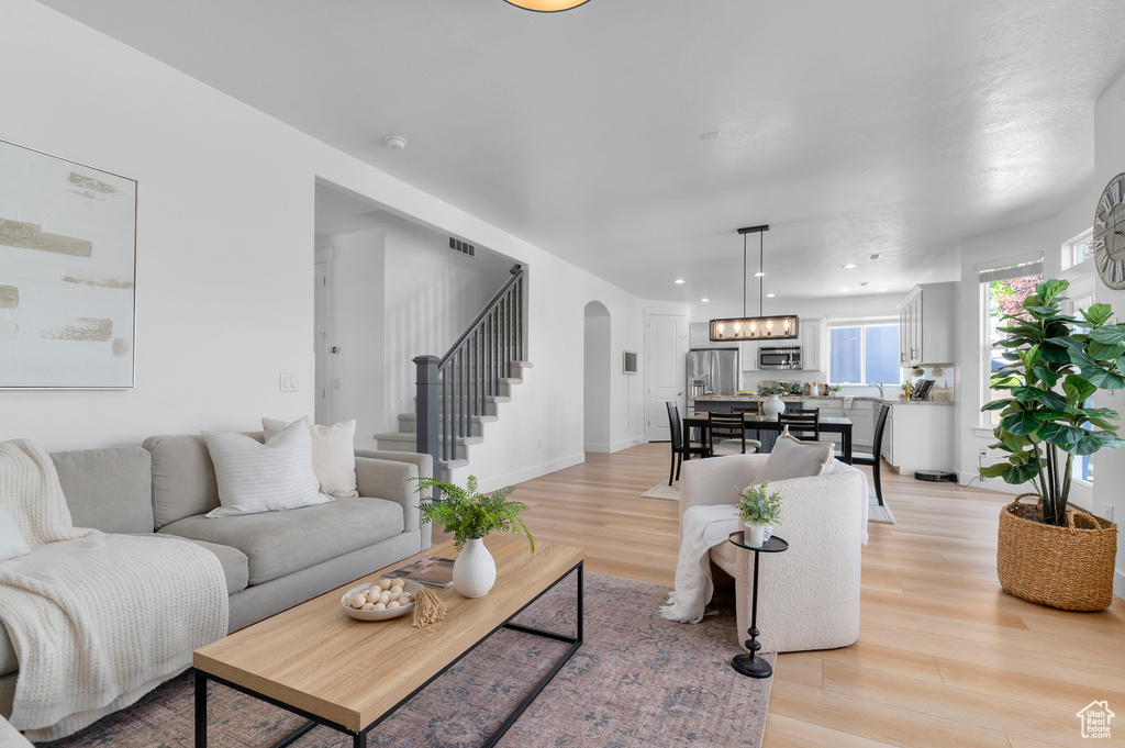 Living room with arched walkways, light wood-style floors, stairs, and recessed lighting