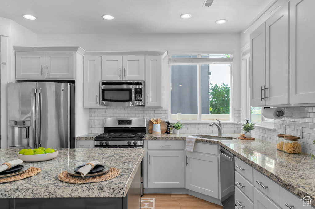 Kitchen with stainless steel appliances, decorative backsplash, light stone counters, recessed lighting, and white cabinets
