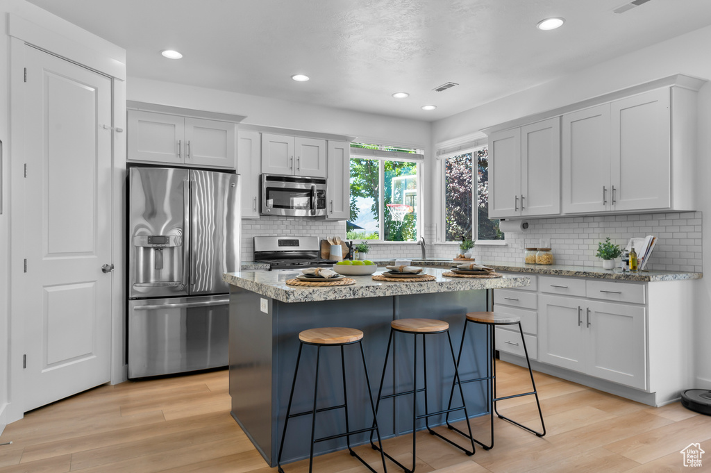 Kitchen with appliances with stainless steel finishes, a kitchen bar, light wood-type flooring, decorative backsplash, and recessed lighting