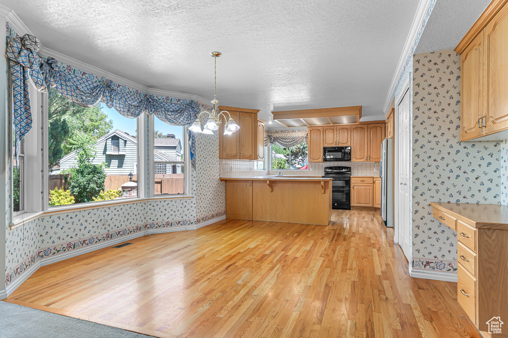 Kitchen with black microwave, wallpapered walls, range, freestanding refrigerator, and light wood-type flooring