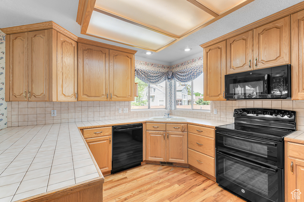 Kitchen with black appliances, tile countertops, light wood-style floors, tasteful backsplash, and recessed lighting