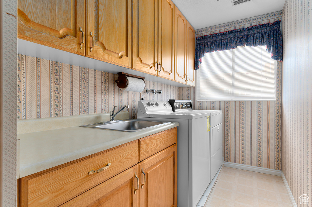 Laundry room with wallpapered walls, cabinet space, washing machine and dryer, and light flooring