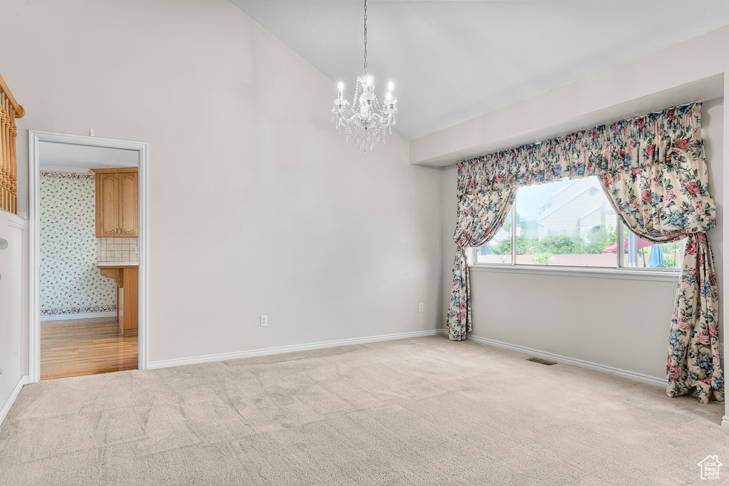 Empty room featuring carpet flooring, a chandelier, and high vaulted ceiling