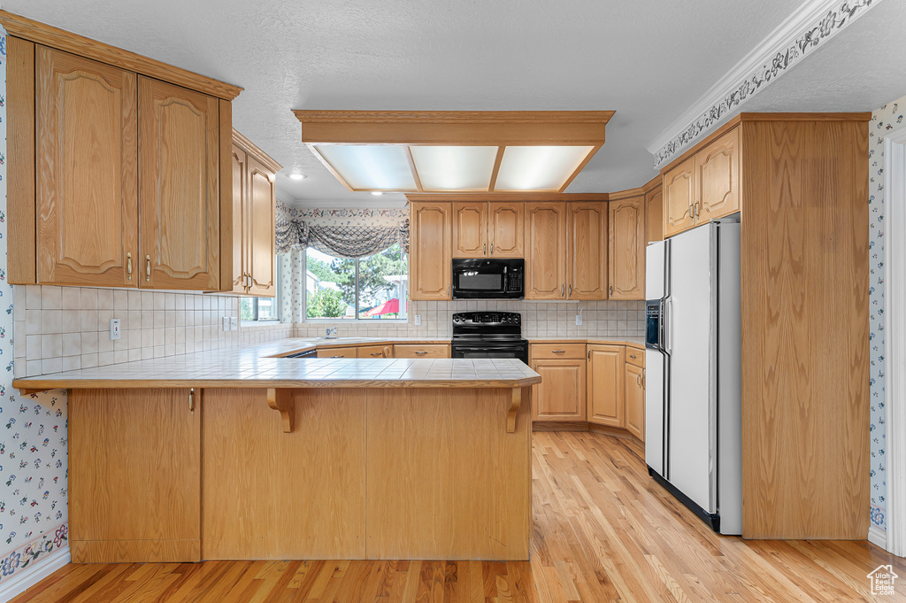 Kitchen with black appliances, a peninsula, light wood-style floors, a kitchen bar, and decorative backsplash