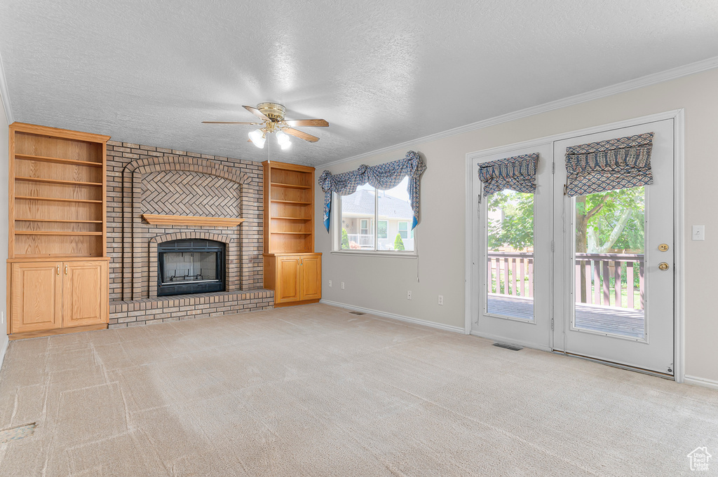 Unfurnished living room with ceiling fan, light colored carpet, a textured ceiling, crown molding, and a fireplace