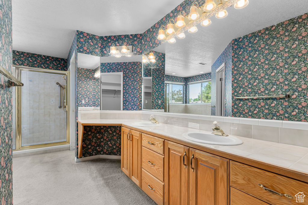 Full bath featuring wallpapered walls, double vanity, a stall shower, and a textured ceiling