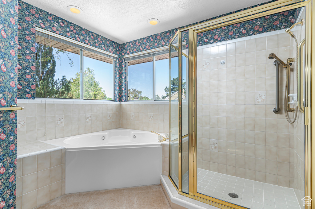 Full bathroom with healthy amount of natural light, a shower stall, a garden tub, wallpapered walls, and a textured ceiling