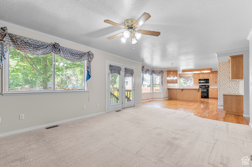 Unfurnished living room with light carpet, crown molding, ceiling fan, a textured ceiling, and light wood finished floors