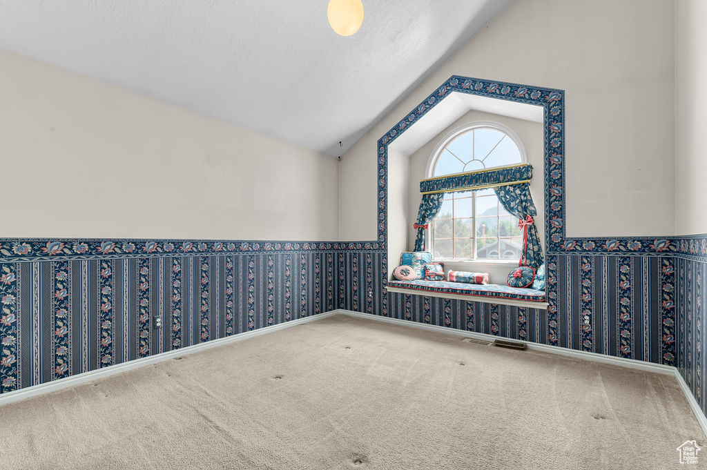 Empty room with lofted ceiling, carpet floors, and wallpapered walls