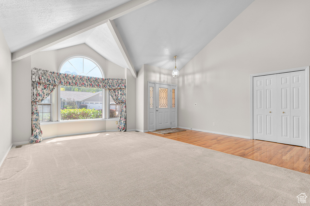 Unfurnished living room featuring carpet floors, high vaulted ceiling, beam ceiling, and a chandelier
