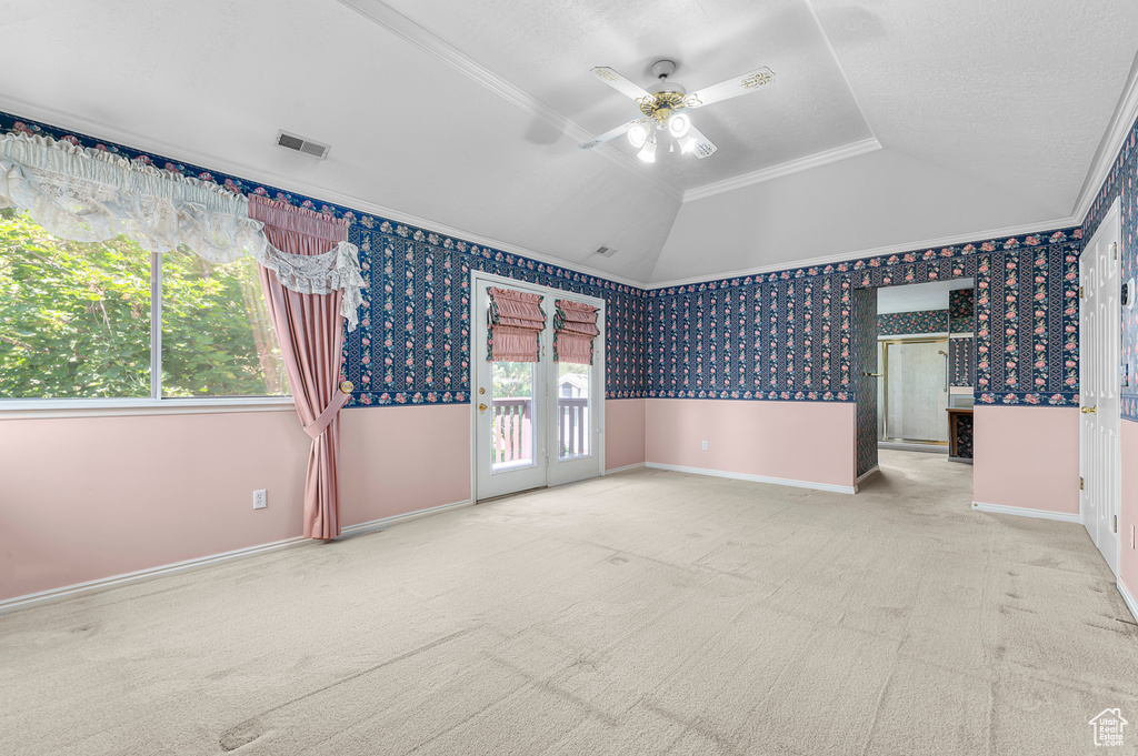 Carpeted empty room featuring ceiling fan, crown molding, vaulted ceiling, and wallpapered walls