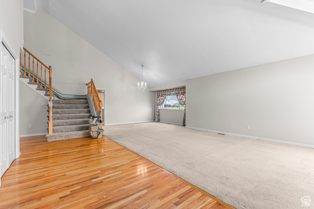 Unfurnished living room with stairway, a chandelier, wood finished floors, carpet floors, and high vaulted ceiling