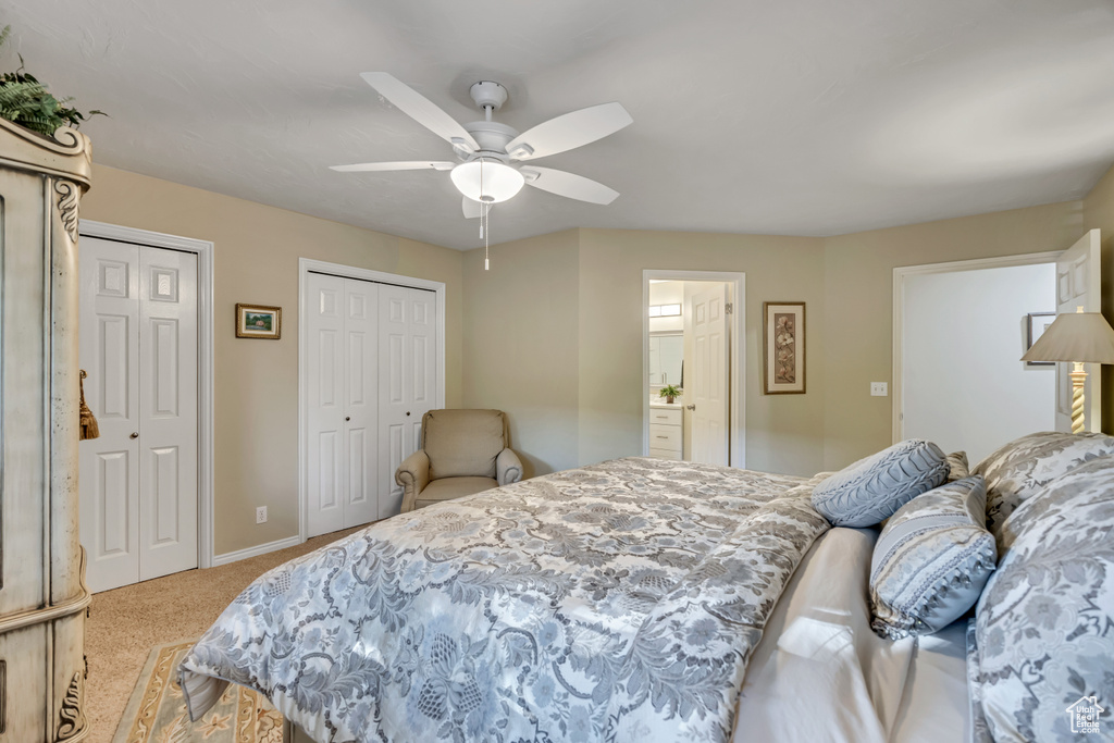 Bedroom featuring multiple closets, light colored carpet, ceiling fan, and ensuite bathroom