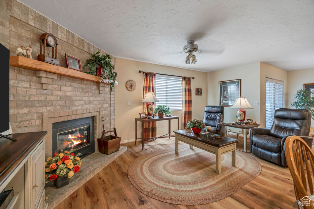 Living room with a ceiling fan, a brick fireplace, light wood-style flooring, and a textured ceiling