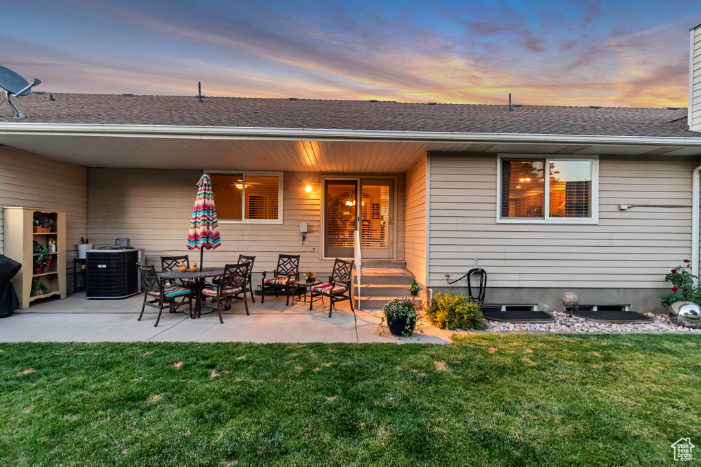 Back of property at dusk featuring a lawn, a patio, and roof with shingles
