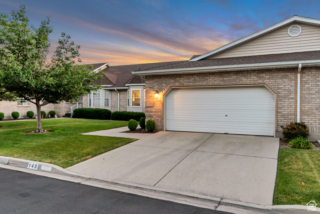 View of front of house featuring a front yard, driveway, an attached garage, brick siding, and roof with shingles